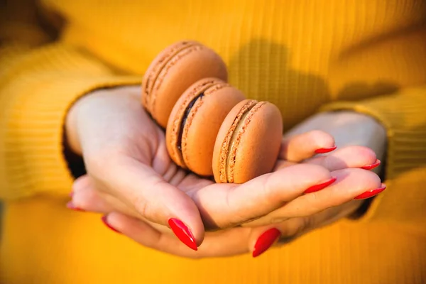 Frauenhände, die leckere Macarons aus nächster Nähe halten. Herbststimmung, Mode und Lifestyle. Orangen Macarons zum Herbstfest — Stockfoto