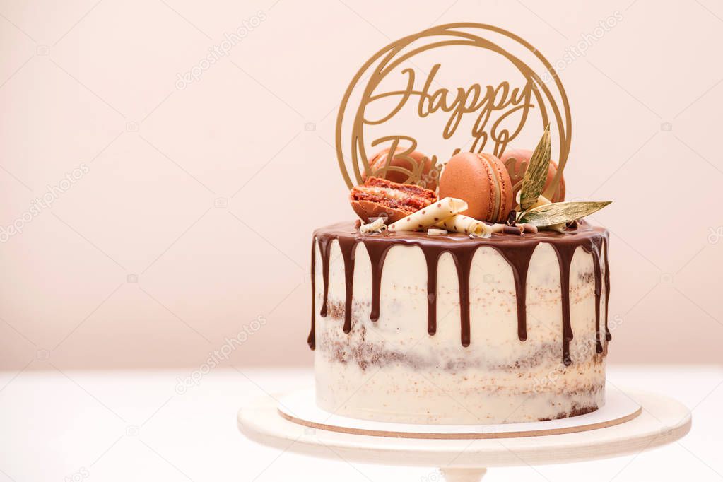 Birthday cake decorated with golden macaroons and chocolate pieces. Elegant naked cake topped by chocolate. 