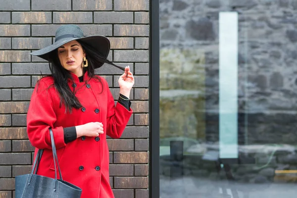 Preciosa mujer de moda caminando por la calle. Chica vestida con elegante abrigo rojo y sombrero de moda negro. Moda, belleza, maquillaje . — Foto de Stock