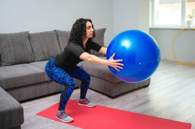 Sportif kadın fitball 'la çömelme egzersizi yapıyor. Sportif, sağlıklı bir yaşam tarzı. Ev ödevi konsepti. Fitness egzersizi. Evde kız eğitimi. Spor giyim sektöründe güçlü bir kız.