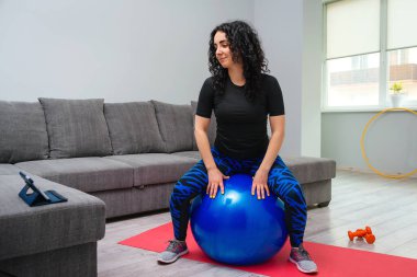 Evde kız eğitimi. Spor giyim sektöründe güçlü bir kız. Sportif kadın fitball ile egzersiz yapıyor. Sportif, sağlıklı bir yaşam tarzı. Ev antrenmanı. Fitness egzersizi. Tabletten online ders izleyen kız.