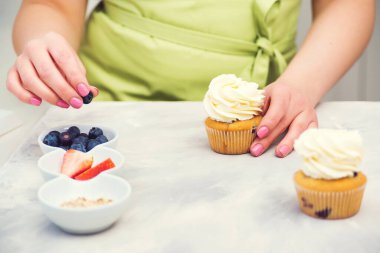Şekerci yaban mersinli kek dekore ediyor. Yemek kursu, aşçılık ve fırın. Tatlılar. Şekerci kekleri krem peynirle dekore eder, yakın plan. Ev yapımı hamur işi. Pasta pişiren kadın.