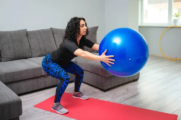 身材矮小的女人带着皮球做蹲姿练习 健康的生活方式 家庭锻炼的概念 健身锻炼 女孩在家里训练 穿着运动服的强壮的女运动员 — 图库照片