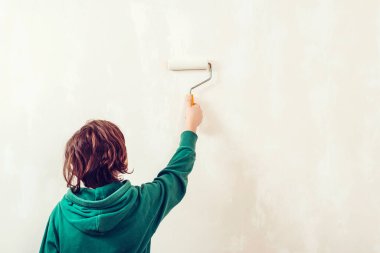 Boyalı silindirli şirin bir çocuk. Mutlu çocuk ebeveynlerin duvar boyamasına yardım eder. Aile için yeni bir ev. Ev tadilatı. Çocuk tadilat sırasında eğleniyor. Genç çocuk boya silindiriyle iç duvarı boyuyor..