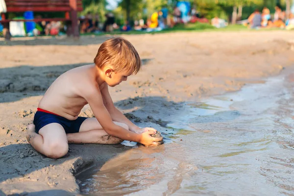 Little boy play with sand on summer beach. Funny games during summer vacation. Child having fun with sand at coast. Sunny summer day. Leisure, games and vacation. Cute kid playing game at the beach.