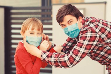Maskeli bir baba ve oğlu sokakta yürüyor. Dışarıda maske takan bir aile. Koronavirüsü önleme. Coronavirus karantinası. Yeni gerçek hayat. Coronavirüs salgını.
