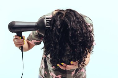 Woman makes herself curly hairstyle. Girl using a modern hairdryer. Haircare concept. Woman drying hair at home. Woman styling her curly hair with hairdryer with special diffuser nozzle. clipart