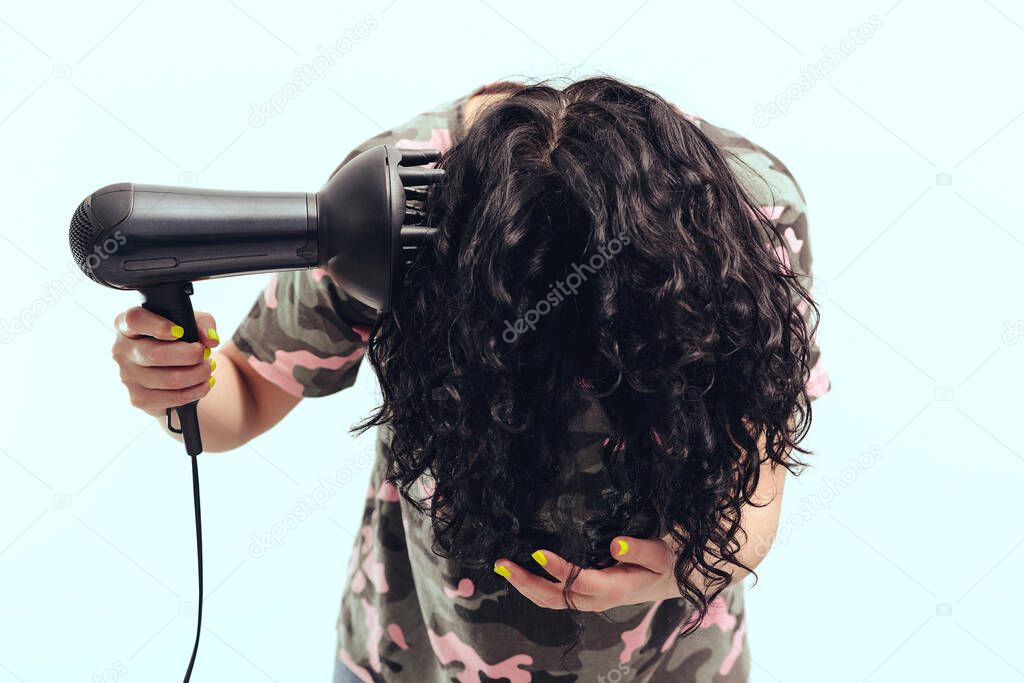Woman makes herself curly hairstyle. Girl using a modern hairdryer. Haircare concept. Woman drying hair at home. Woman styling her curly hair with hairdryer with special diffuser nozzle.
