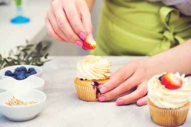 Profesyonel şekerlemeci kekin üstünü çilekle süslüyor. Ev yapımı hamur işi. Pasta pişiren kadın. Şekerci kekleri krem peynirle dekore eder, yakın plan. Kekler, şekerlemeler. Tatlılar.