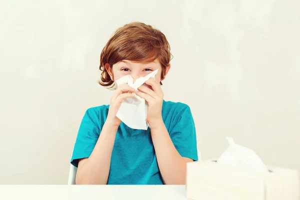 鼻水を吹く小学生 病気の少年は机に座っている 紙ナプキンを使って子供 アレルギーの子供 インフルエンザの季節 子供は鼻をナプキンで拭く 男の子にはウイルス 頭痛があります — ストック写真