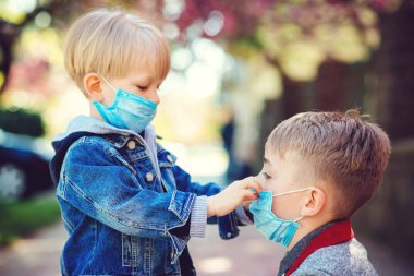 Dışarıda maskeli çocuklar var. Koronavirüsü önleme. Okula dönelim. Coronavirus karantinası. Erkek kardeş, küçük kardeşine yüz maskesi takmasına yardım eder. Aile yürüyüşe çıktı..