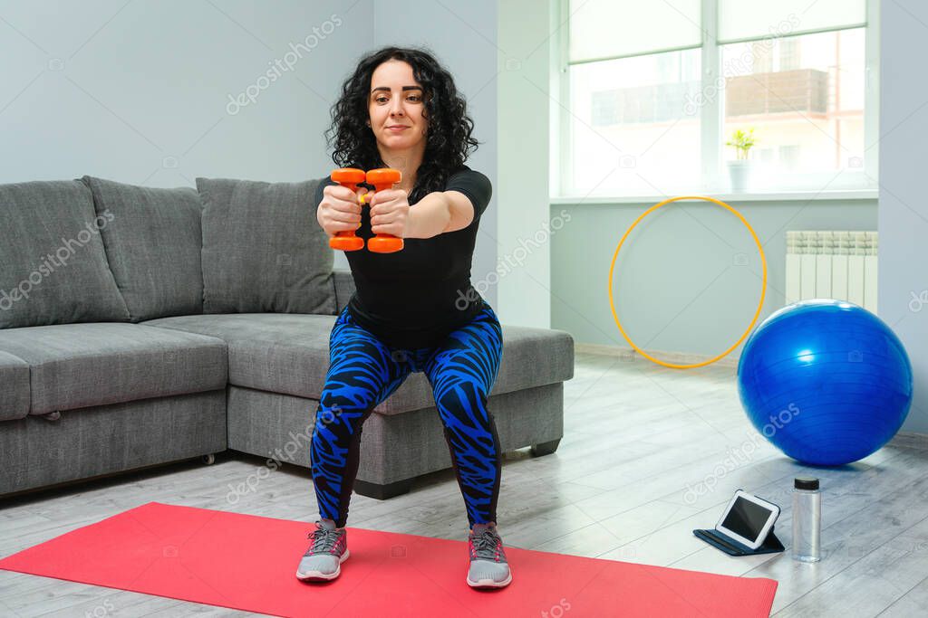 Woman exercising with dumbbells at home. Sport, fitness and recreation concept. Girl training at home. Woman want to stay fit. Young girl doing exercises at room. Beautiful woman squats with dumbbells.