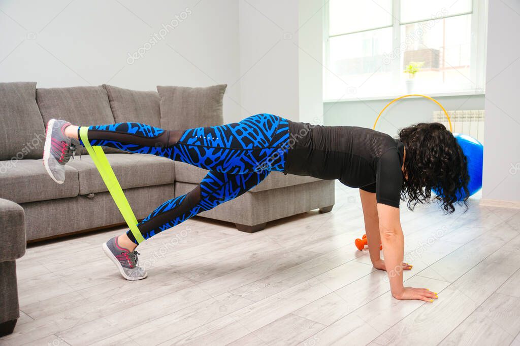 Home workout with resistance band. Girl training at home. Sports woman exercising with resistance band. Strong sporty girl in sportswear. Fitness exercise. Girl watching online tutorials on tablet.