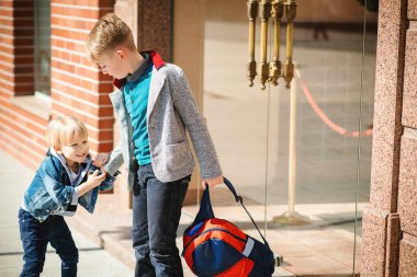 Sırt çantalı okul çocukları okula gidiyor. Dışarıda şık kardeşlerim var. Okul konseptine geri dönelim. Arkadaşlar, çocukluk ve eğitim. İlkokul. Sokaklardaki moda çocukları..