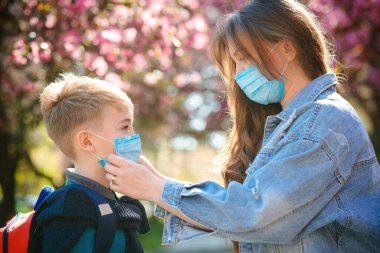 Anne oğluna güvenlik maskesi takıyor. Sırt çantalı tatlı çocuk okula gidiyor. Okul konseptine geri dönelim. Coronavirus karantinası. Öğrenci çocuk okula gitmeye hazır. Koronavirüs dünya salgını.