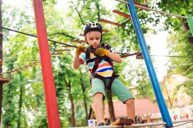 Halat parkındaki küçük çocuk engelleri aştı. Sevimli çocuk ip yoluna tırmanıyor. Yüksek tel parka tırmanma macerası. Kask takan ve güvenlik ekipmanı olan çocuk. Macera parkında ekstrem spor.