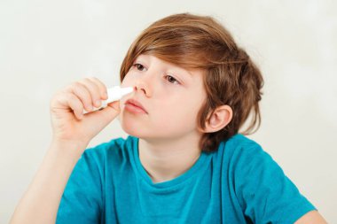 Burnu akan hasta çocuk burun spreyi kullanıyor. Burun alerjisi. Hastalık tedavisi sezonu olan bir çocuk. Alerjik çocuk, grip mevsimi. Çocuğun virüsü var, burnu akıyor ve başı ağrıyor. Burnu akan bir öğrenci.