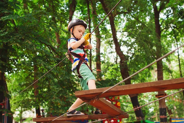 Little boy in the rope park pass obstacles. Cute kid climb the rope road. Adventure climbing high wire park. Boy wearing helmet and safety equipment. Extreme sport in adventure park.