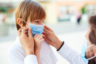 Baba oğluna koronavirüsü korumak ve önlemek için maske takıyor. Babam ve okul çocuğu yüz maskesi takıyor. Öğrenci çocuk okula gitmeye hazır. Küçük çocuk koronavirüs salgını sırasında okula gidiyor..