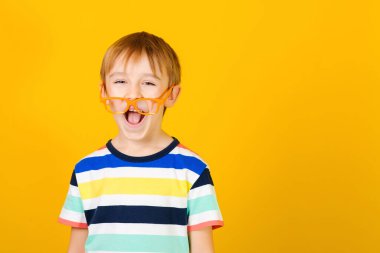 Sarı arka planda gözlüklü zeki çocuk. Pozitif duygu ve yüz ifadesi. Gözlüklü çocuk bağırıyor. Komik küçük okul çocuğu bağırıyor. Boşluğu kopyala.