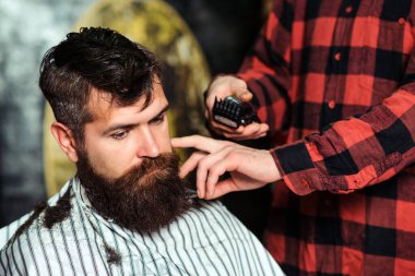 Sakallı yakışıklı adam kuaförü ziyaret ediyor. Berber dükkanı. Sakallı hippi saç stili yapıyor. Müşteriye hizmet eden erkek kuaför. Berber saç kesimini makina ve tarak kullanarak yapıyor. Kuaförde şık sakallı adam.