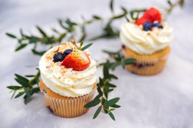 Krem peynir, yabanmersini ve çilekle süslenmiş lezzetli kekler. Modern beton arka planda meyveli kekler. Tatlı hamur işi. Meyveli tatil kekleri. Parti için tatlı kekler..