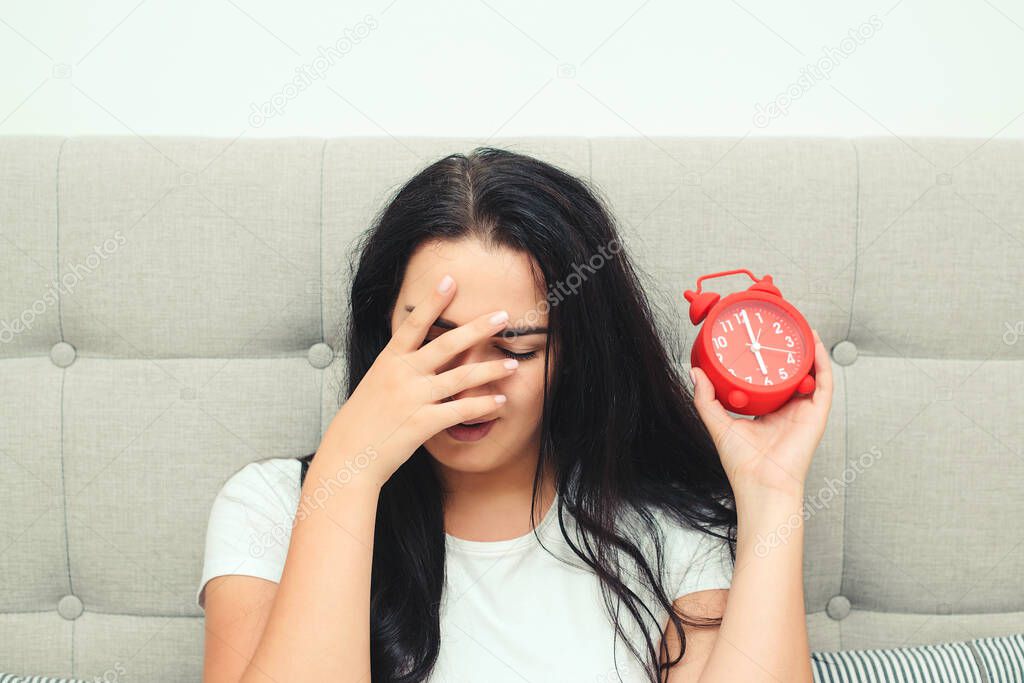 Overslept woman with alarm clock in bed. Early morning awaking. It is time to waking up. Red alarm clock. Young sleeping woman and alarm clock in bedroom.