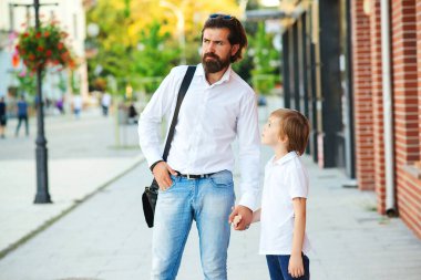 Şık bir baba ve oğul sokakta el ele tutuşuyor. Baba oğluyla dışarıda konuşuyor. Mutlu aile okuldan sonra eve gidiyor. Moda, babalık ve ilişki. Modaya uygun baba ve çocuk..