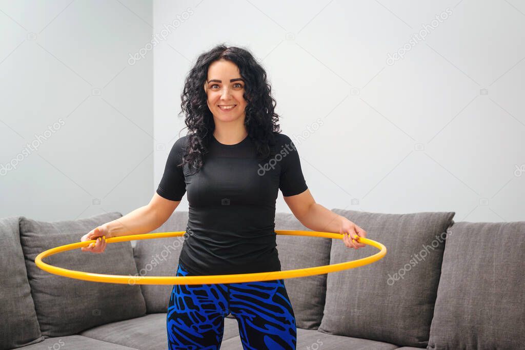 Woman rotating hula hoop. Girl training at home. Healthy sporty lifestyle. Woman doing workout and works with hula hoop. Happy fitness woman. Waist building and weight loss concept.