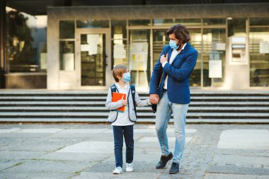 Babam ve okul çocuğu yüz maskesi takıyor. Coronavirus salgını sırasında okula döndüm. Baba ve oğul okuldan sonra eve gidiyor. Öğrenci, çivi çakarken güvenlik maskesi takıyor. Coronavirus karantinası.
