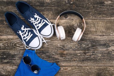 Ahşap arka planda kulaklık ve spor ayakkabılar. Moda erkek aksesuarları, üst manzara. Moda ayakkabıları, güneş gözlükleri ve modern kablosuz kulaklıklar. Erkek modası. Uzayı kopyala Hippi kentsel tarzı