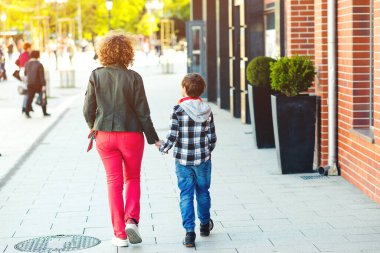 Anne ve oğlu el ele tutuşuyorlar. Anne ve çocuk şehirde yürüyor. Mutlu aile birlikte vakit geçiriyor. Annelik, ilişki ve aile kavramı.