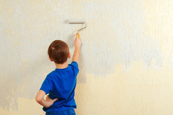 Cute child holding paint roller. Happy kid helps parents to paint wall. New house for family. Home renovation. Boy having fun during home renovation. Young boy painting interior wall with paint roller.