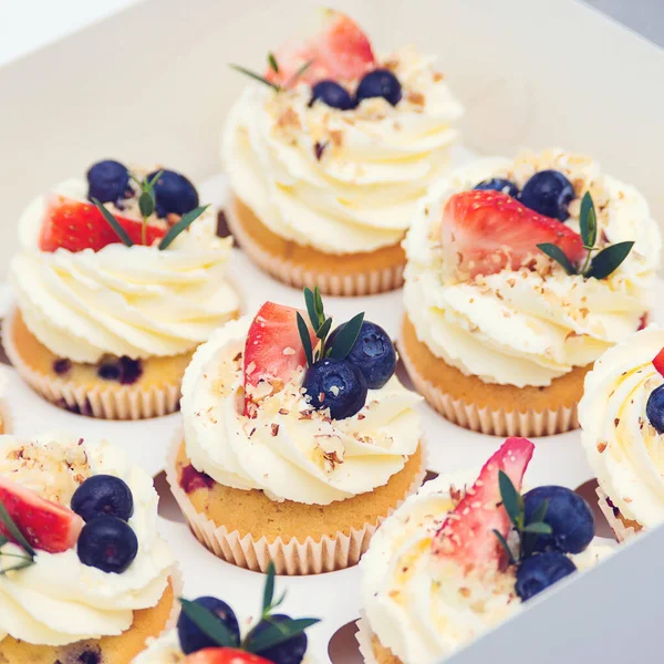 Holidays cupcakes with strawberry and blueberry, close up. Cupcakes packaging, delivery box. Gift box with sweets. Sweet shop. Present box full of fruit cupcakes.