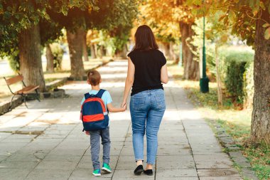 Anne çocuğu okula götürüyor. Okuldaki ilk günüm. Annem birinci sınıfta küçük bir çocuğu yönetiyor. İlkokulun ebeveynleri ve öğrencileri el ele gider. Sırt çantalı kadın ve çocuk..
