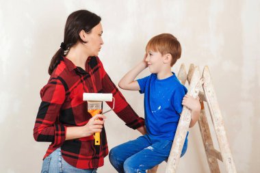 Mutlu aile anne ve oğlu duvarı boyuyor. Apartmanda tamirat var. Genç bir aile birlikte evlerini yeniliyorlar. Anne ve çocuk boya silindiriyle duvar boyuyor..