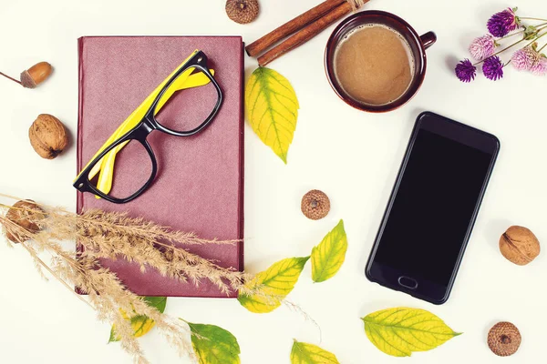 Autumn background with cup of coffee, book, mobile phone and autumn leaves. Mockup with smartphone and autumn decoration. Autumn time for reading.