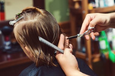 Berber dükkanında saç tıraşı olan sevimli küçük bir çocuk. Berber çocuk saç modelini yapıyor. Makasla kuaför. Berber dükkanı. Çocukluk. Genç çocuk için yeni saç stili.