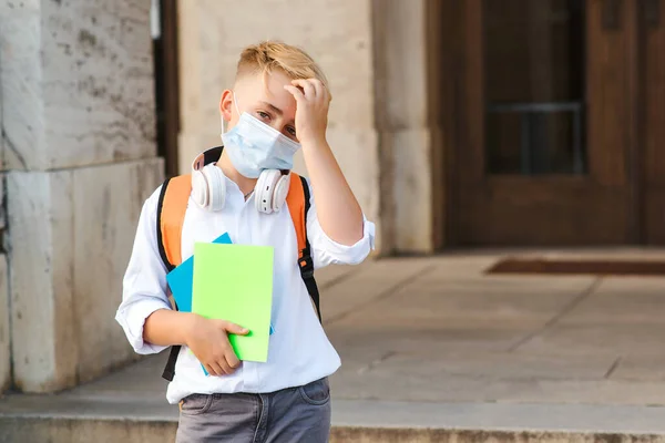 School boy wearing face mask during corona virus outbreak. Boy going back to school after covid-19 quarantine. Boy in safety mask for coronavirus prevention. Kid with backpack going to school.