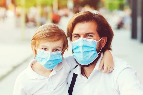 Father with child in medical mask at city. Stylish dad and son walking at street during quarantine. Face mask to protection from coronavirus. Healthy and safety childhood. Schoolboy in face mask.