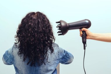 Hairdresser makes curly hairstyle for woman. Haircare concept. Woman styling her curly hair with hairdryer with special diffuser nozzle. Girl using a modern hairdryer. clipart