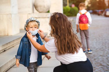 Anne, küçük oğlu için açık havada tıbbi maske takıyor. Coronavirus ve gerçek hayat. Koronavirüsü önlemek için tıbbi maske. Coronavirus karantinası. Aile yürüyüşe çıktı..