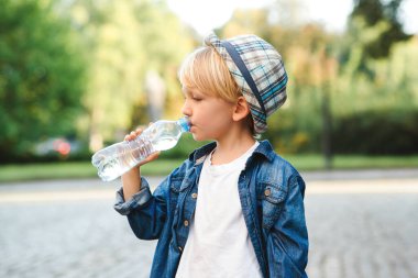 Plastik şişeden su içen şirin bir çocuk. Çocuk dışarıda su içiyor. Sokakta maden suyu içen bir çocuk. Sağlıklı çocukluk.