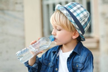 Plastik şişeden su içen şirin bir çocuk. Çocuk dışarıda su içiyor. Sokakta maden suyu içen bir çocuk. Sağlıklı çocukluk.