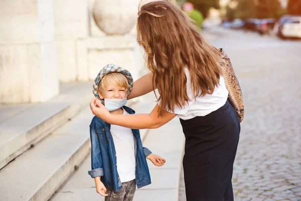 Mother puts on medical mask for little child outdoors. Coronavirus and real life. Medical mask to prevent coronavirus. Coronavirus quarantine. Family on a walk.