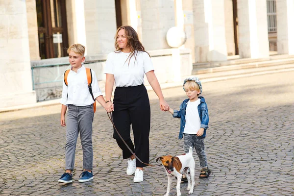 Happy family walking with dog in city street. Stylish mother and kids having fun with their dog outdoors. Little puppy jack russel terrier and owners on a walk. Family, pet and lifestyle. Happy family
