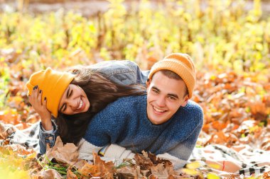 Genç çift sonbaharda birlikte eğleniyor. Sevgi. Sonbaharın tadını çıkaran şık bir çift. Moda, yaşam tarzı ve sonbahar tatili. Sonbahar yapraklarının arasında yatan şık erkek ve kadın..