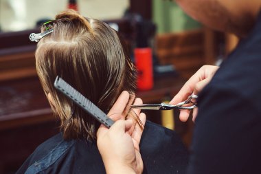 Berber dükkanında saç tıraşı olan sevimli küçük bir çocuk. Berber çocuk saç modelini yapıyor. Makasla kuaför. Berber dükkanı. Çocukluk. Genç çocuk için yeni saç stili.