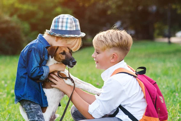 Happy children petting a dog in the park. Lovely kids playing with their dog outdoors. Happiness, friendship, animals and lifestyle. Happy family. Little puppy jack russel terrier and kids.