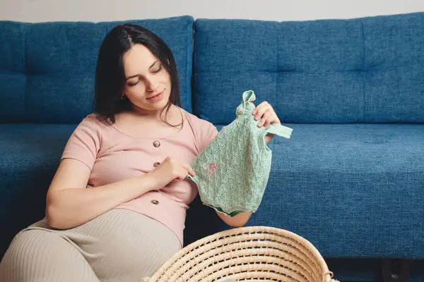 Pregnant woman preparing for baby birth her daughter. Happy mother enjoying pregnancy. Wicker basket of cute tiny stuff newborn. Beautiful pregnant woman at home.